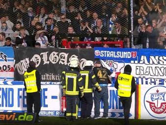 Das Spiel zwischen Verl und Rostock muss zweimal unterbrochen werden. Einmal warfen Fans Gegenstände auf das Spielfeld, dann fängt offenbar ein Gegenstand bei den Gästefans Feuer.