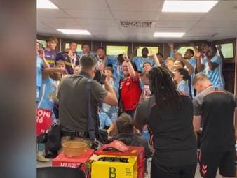 Coventry City feiert nicht nur den Aufstieg in die Premier League, sondern nun auch die Meisterschaft nach einem 3:1 gegen Wrexham. Hinterher taucht ein Überraschungsgast in der Kabine auf: Darts-Liebling Stephen Bunting.