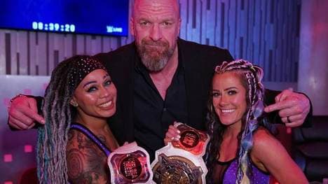 WWE-Vorstand "Triple H" Paul Levesque (M.) posiert mit den neuen Champions Kayden Carter (l.) und Katana Chance