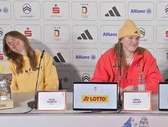 Die deutschen Olympia-Athletinnen Julia Taubitz, Emma Aicher und Kira Weidle-Winkelmann werden auf einer Pressekonferenz zu ihrem Maskottchen befragt - daraufhin bricht Gelächter aus.