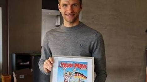 Stolz hält Thomas Müller eine gerahmte Ausgabe in die Kamera.