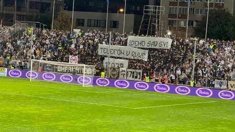 Bosnische Fans halten ein Transparent hoch und schalten ihre Handylichter ein