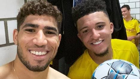 Jadon Sancho (r.) lässt Teamkollege Achraf Hakimi auf dem Spielball unterschreiben